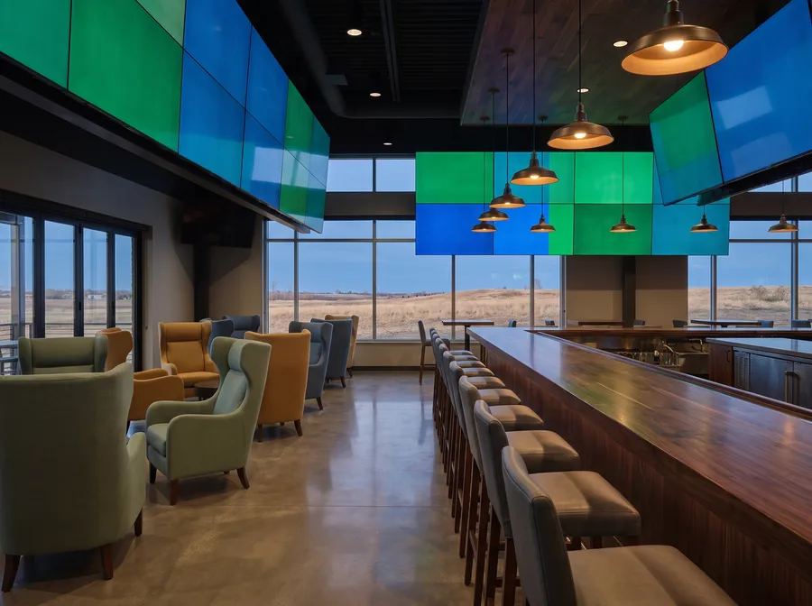 Generated scene: an empty sports bar before opening, with a long wooden bar, stools, armchairs and large screens showing plain colour fields.